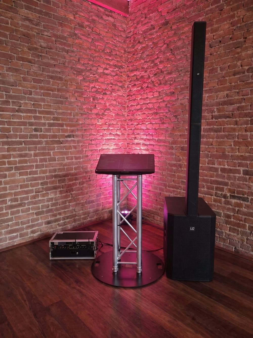 Musiktheke mit Lautsprechersäule vor einer Backsteinwand, in pinkes Licht getaucht